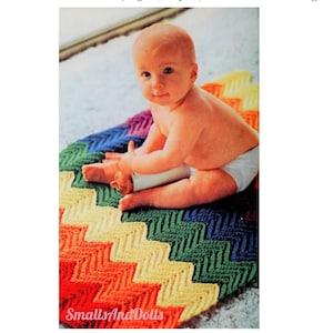May include: A baby sits on a rainbow chevron crochet blanket. The blanket is made with different colored yarn in a zig-zag pattern. The blanket is on a light brown carpet.