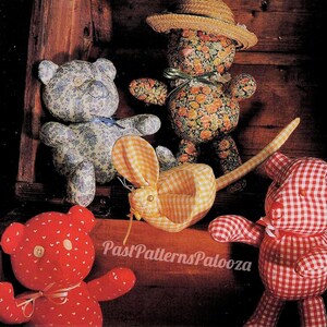 May include: Four handmade stuffed toys: a yellow and white gingham mouse, a red and white gingham teddy bear, a blue and white floral teddy bear, and a floral teddy bear wearing a straw hat. The toys are arranged in a wooden box.