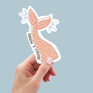 May include: A pink mermaid tail sticker with the text "Basically a Mermaid" on the side. The sticker has a white outline and blue water droplets.