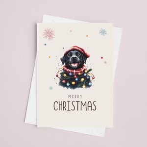 May include: A black Labrador Retriever wearing a red Santa hat and a red and black plaid scarf with Christmas lights around its neck. The card says "Merry Christmas".