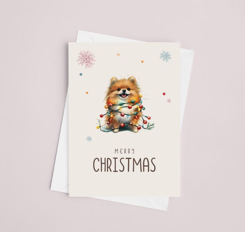 May include: A Christmas card featuring a cute brown and white Pomeranian dog wrapped in colorful Christmas lights. The card has a white background with a light brown border and the text "Merry Christmas" in black.