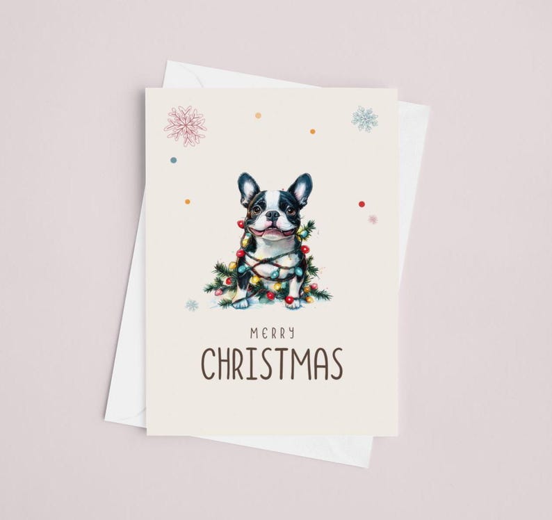 May include: A Christmas card featuring a black and white French bulldog wrapped in colorful Christmas lights. The card has a cream background with a light brown border and the text "Merry Christmas" in black.