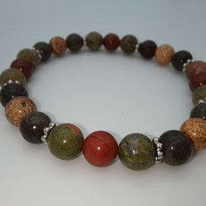 Peut inclure: Un bracelet de perles composé de pierres aux tons terreux, notamment des nuances de marron, de vert, de rouge et de beige. Les perles rondes sont séparées par des entretoises argentées. Le bracelet est présenté sur fond blanc.