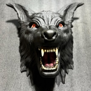 May include: A black wolf head sculpture with a snarling expression and glowing red eyes. The sculpture is mounted on a gray wall.