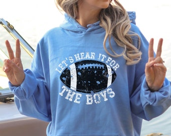 Op de afbeelding: Een lichtblauwe hoodie met een verweerde witte afbeelding van een voetbal en de tekst "Let's hear it for the boys".