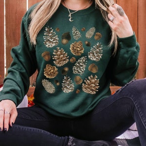 May include: A dark green sweatshirt with a pattern of brown and beige pine cones and acorns.