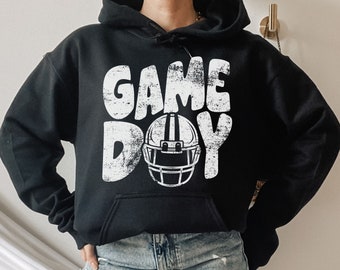 Könnte beinhalten: Schwarzer Hoodie mit einer weißen Grafik, auf der "GAME DAY" steht, mit einem Footballhelm in der Mitte des Textes.