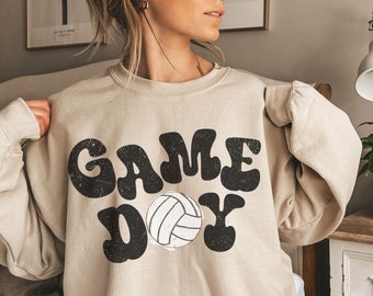 May include: A beige sweatshirt with the text "GAME DAY" in black with a stylized volleyball graphic.