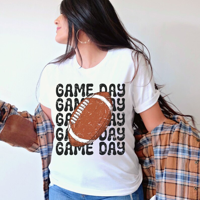 May include: White t-shirt with a brown and white football graphic and the text "GAME DAY" repeated in a retro style.