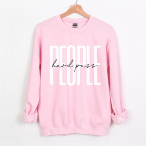 Puede incluir: Sudadera rosa con el texto "PEOPLE hard pass" en letras blancas.