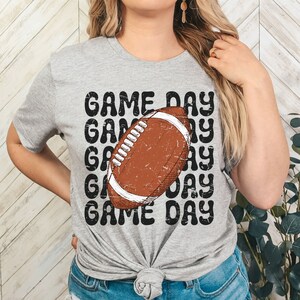 May include: Gray t-shirt with a distressed black graphic of a football and the text "GAME DAY" repeated multiple times.