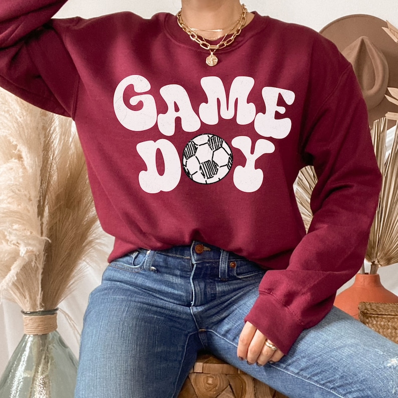 May include: A maroon sweatshirt with the words "GAME DAY" in white retro font and a black and white soccer ball graphic.
