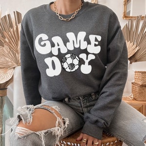 May include: A gray sweatshirt with the text "GAME DAY" in white with a white soccer ball graphic.