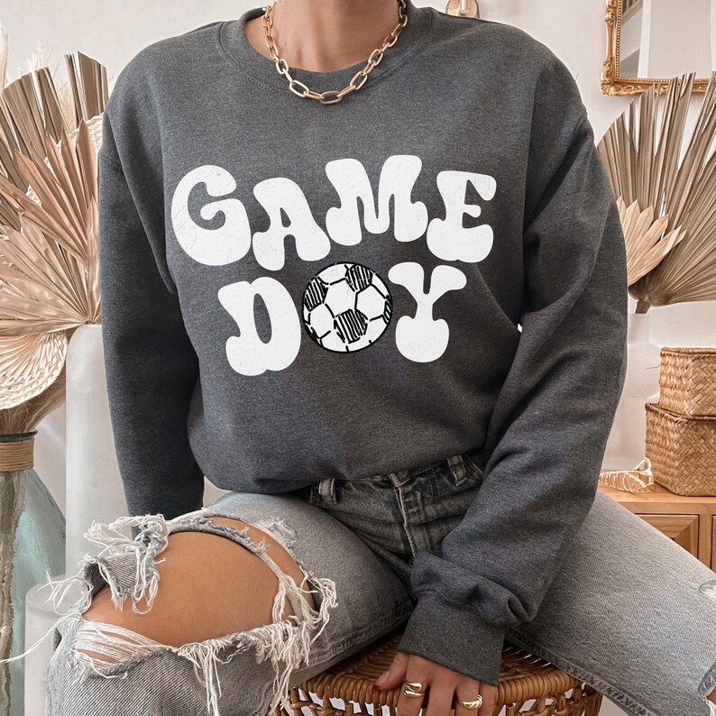 May include: A gray sweatshirt with the text "GAME DAY" in white with a white soccer ball graphic.