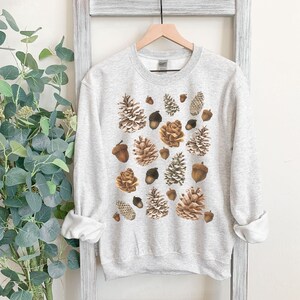 May include: A light gray sweatshirt with a pattern of brown pine cones and acorns.