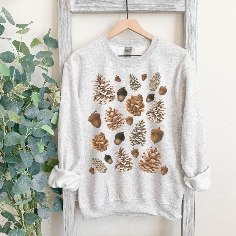 May include: A light gray sweatshirt with a pattern of brown pine cones and acorns.
