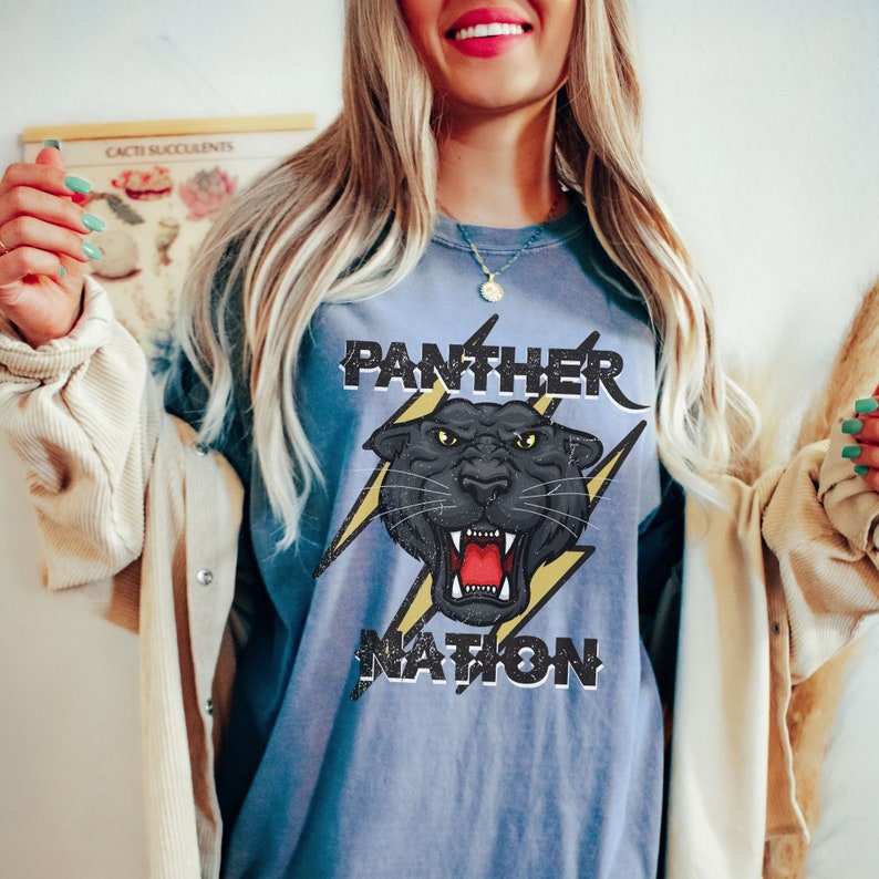 Op de afbeelding: Een blauw T-shirt met een zwarte panter afbeelding en de tekst "Panther Nation" in een verweerd lettertype.