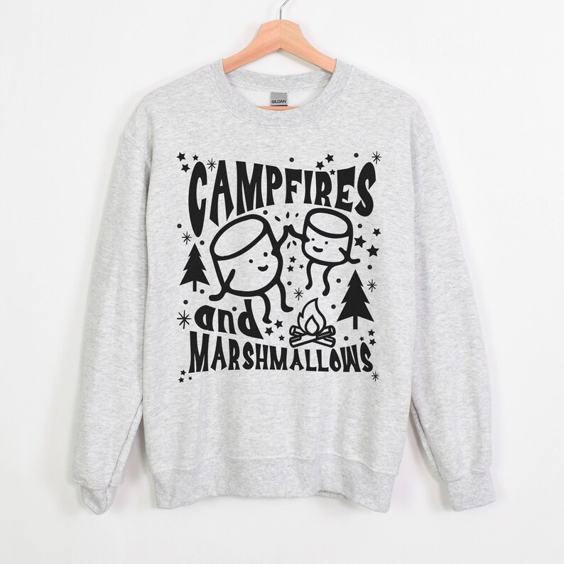 Puede incluir: Sudadera gris con un dise&ntilde;o gr&aacute;fico negro de dos malvaviscos de dibujos animados tom&aacute;ndose de la mano frente a una fogata con el texto "Campfires and Marshmallows".
