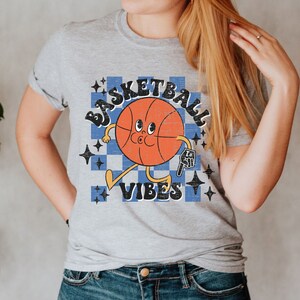 May include: A gray t-shirt with a retro-style basketball graphic. The basketball has a face and is holding a basketball. The text "Basketball Vibes" is printed below the basketball.