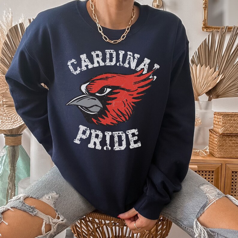 Op de afbeelding: Een marineblauw sweatshirt met een rode kardinaalvogel afbeelding en de tekst "CARDINAL PRIDE" in witte, verweerde letters.