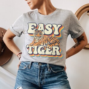 May include: A grey t-shirt with a retro-style graphic of a tiger and the text "EASY TIGER" in rainbow colours.