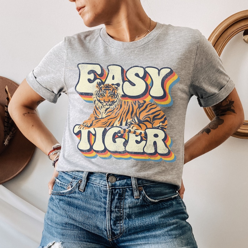 May include: A grey t-shirt with a retro-style graphic of a tiger and the text "EASY TIGER" in rainbow colours.