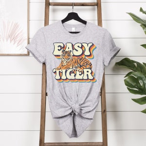 May include: Grey t-shirt with a retro-style graphic of a tiger and the text "EASY TIGER" in rainbow colours.