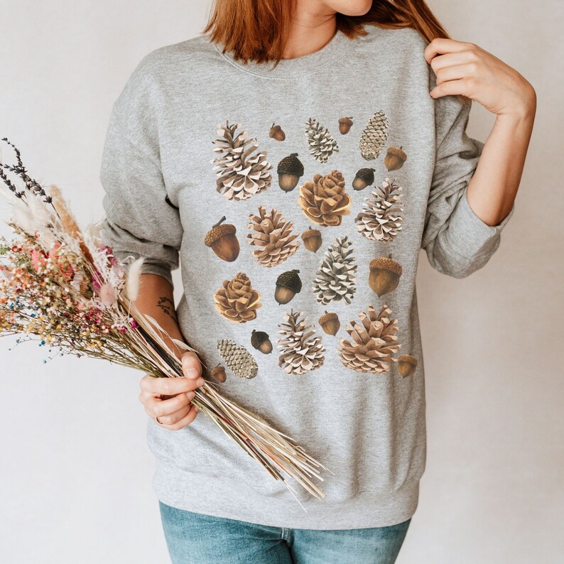 May include: A gray sweatshirt with a pattern of brown pine cones and acorns.