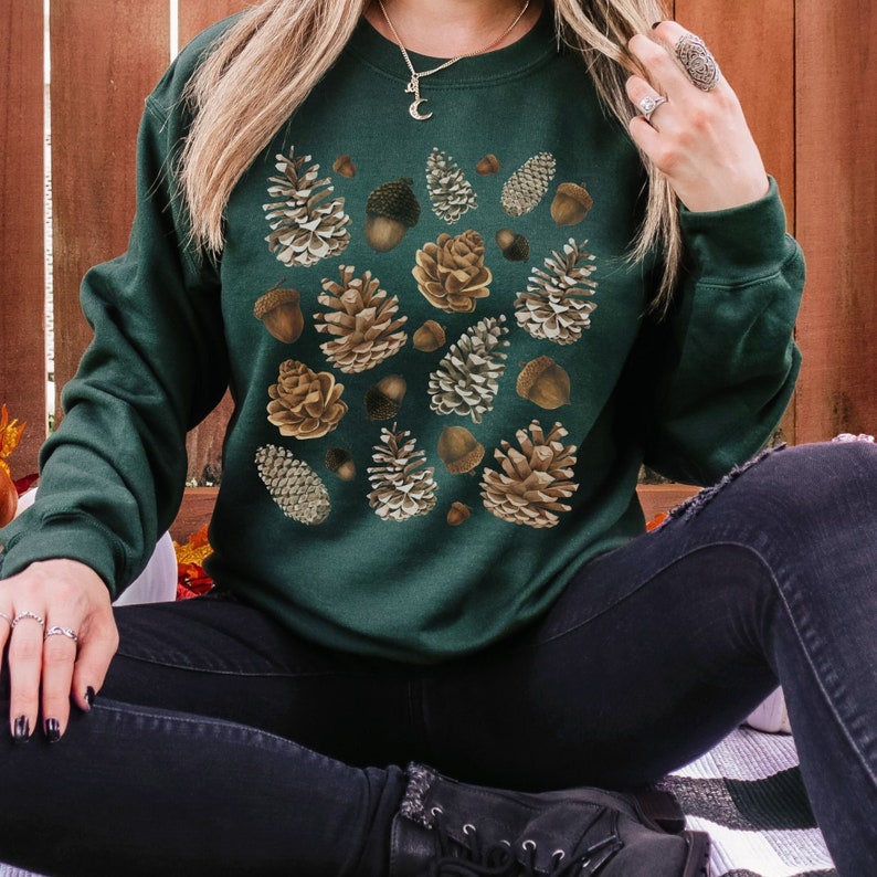 May include: A dark green sweatshirt with a pattern of brown and beige pine cones and acorns.