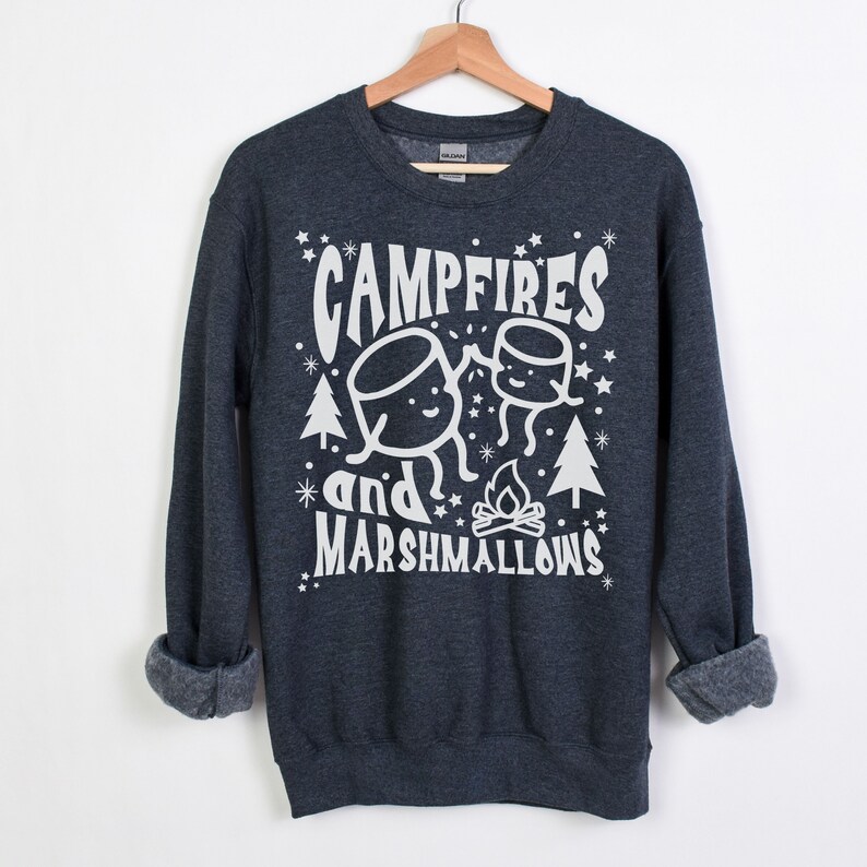 Puede incluir: Una sudadera gris oscuro con un dise&ntilde;o gr&aacute;fico blanco que dice "Campfires and Marshmallows" con una imagen de dibujos animados de dos malvaviscos y una fogata.