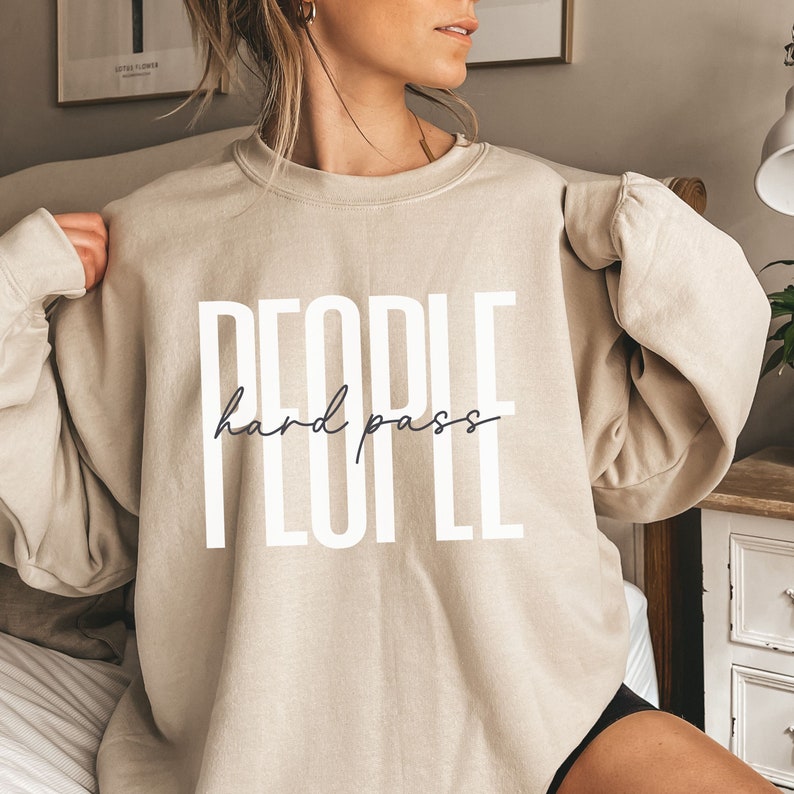Puede incluir: Una sudadera beige con el texto "PEOPLE hard pass" impreso en blanco en la parte delantera.