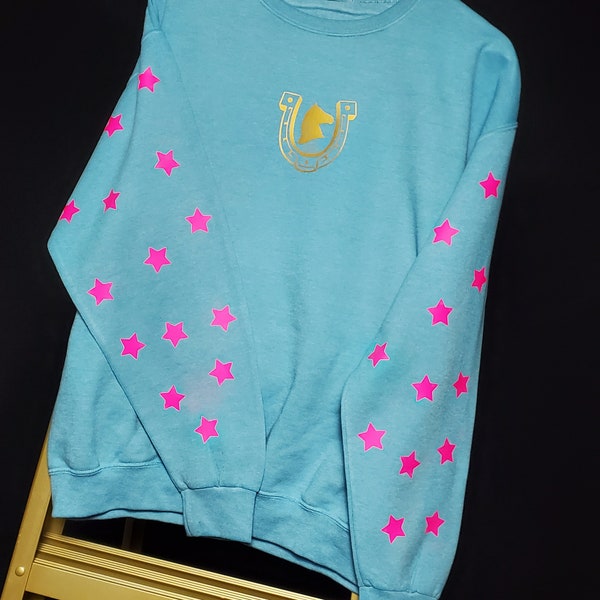 Aqua dyed prewashed sweatshirt with pink fluorescent/glow in the dark stars on sleeves and gold horse and horseshoe on chest