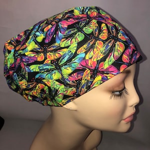 May include: A black scrub hat with a colorful dragonfly print. The hat has a bright yellow, green, blue, pink, and orange dragonfly pattern.