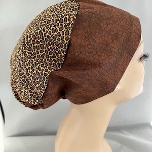 May include: Brown and leopard print scrub hat with a gathered top. The hat is made of a soft, comfortable fabric and is perfect for nurses, doctors, and other healthcare professionals.