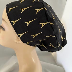 May include: Black scrub cap with a gold Eiffel Tower pattern. The cap is made of a soft fabric and is designed to fit comfortably. The Eiffel Tower design is repeated across the entire cap.