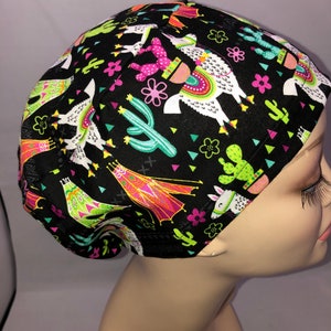 May include: Black scrub hat with a colorful llama and cactus print. The hat has a tie at the back.