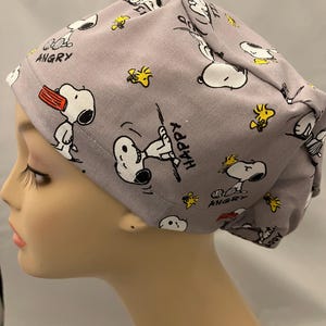 May include: A gray scrub hat with a repeating pattern of Snoopy characters and the words "Angry" and "Happy".