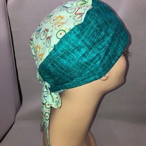 May include: A turquoise and light green surgical scrub hat with a tie. The hat has a pattern of colorful bicycles on the light green side.