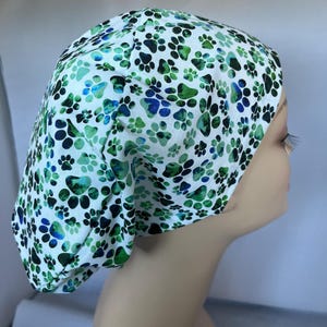 May include: A white scrub cap with a green and blue paw print pattern. The cap is made of a soft, comfortable fabric and is perfect for nurses, doctors, and other healthcare professionals.