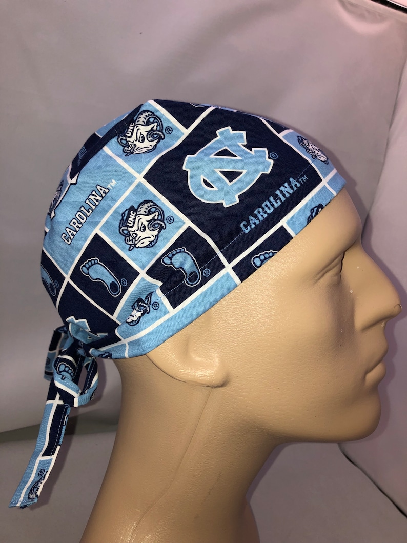 Pu&ograve; includere: Un berretto chirurgico blu e bianco con motivo a fantasia con il logo dei Tar Heels dell'Universit&agrave; della Carolina del Nord e il testo "Carolina TM".