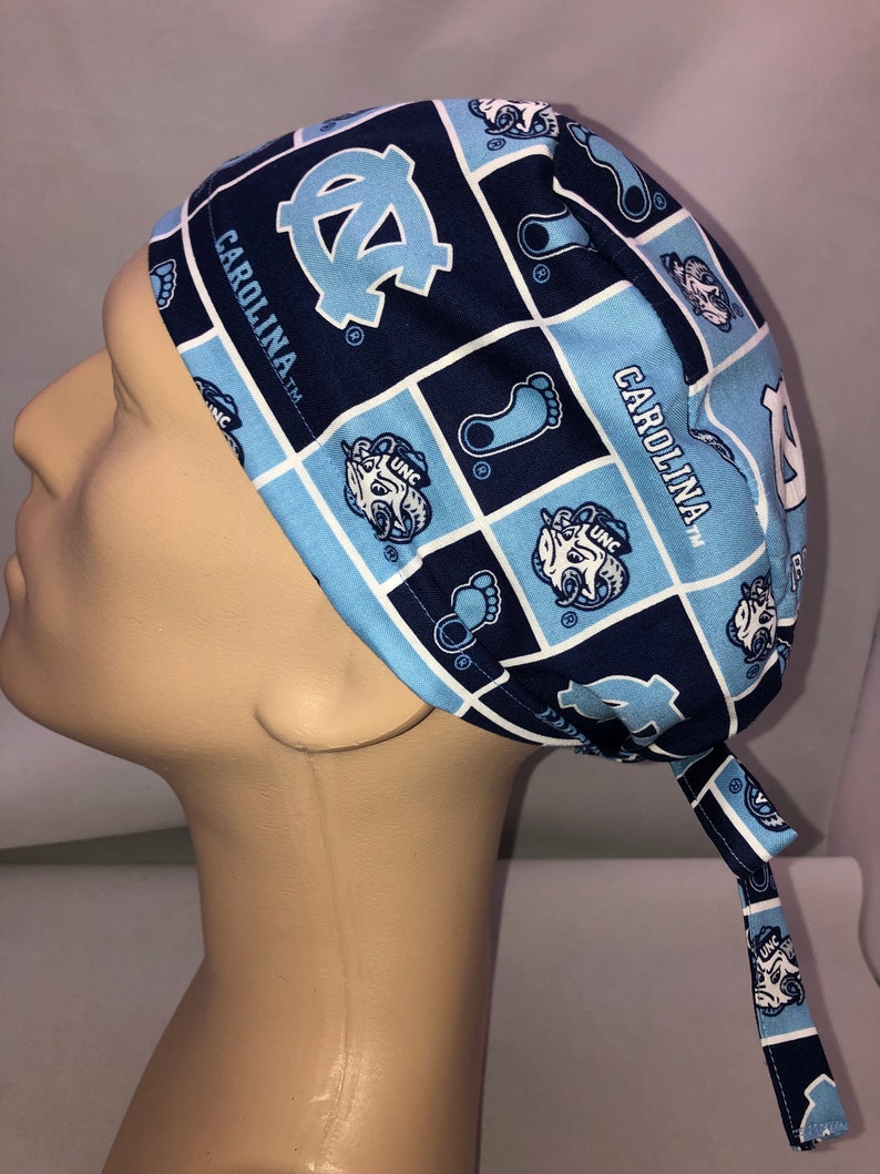 Pu&ograve; includere: Un berretto chirurgico blu e bianco con motivo a fantasia con il logo dei Carolina Tar Heels e il testo "Carolina TM".