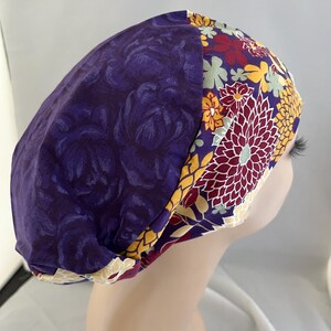 May include: Purple and floral patterned scrub hat with a contrasting floral design on the side. The hat is made of soft, comfortable fabric and is perfect for healthcare professionals.