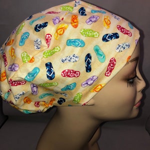 May include: A yellow scrub hat with a colorful flip-flop print. The hat is made of a soft, comfortable fabric and is perfect for nurses, doctors, and other healthcare professionals.