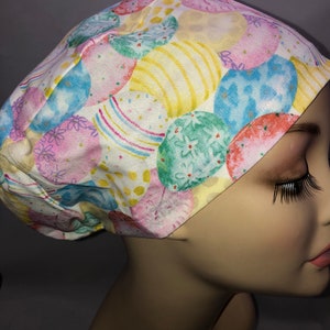 May include: A white scrub hat with a colorful Easter egg pattern. The eggs are in shades of pink, blue, green, and yellow.