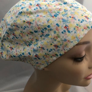 May include: A white scrub hat with a colorful abstract print featuring blue, yellow, pink, and red accents.