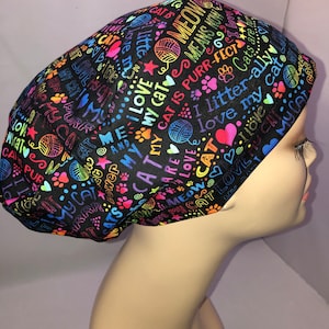 May include: Black scrub hat with a colorful print of cat-themed words and paw prints. The words include "My Cat is Purr-fect", "I Love My Cat", "Meow", and "Cats are the Best".