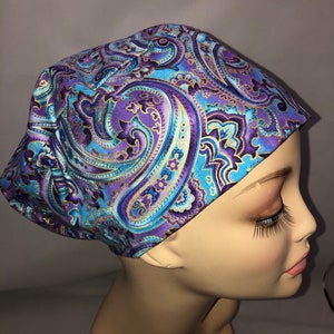 May include: A purple, blue, and gold paisley patterned scrub hat. The hat is made of a soft, comfortable fabric and is perfect for nurses, doctors, and other healthcare professionals.