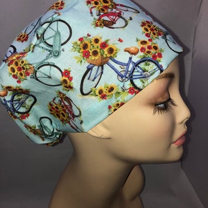 May include: A light blue scrub hat with a repeating pattern of sunflowers and bicycles. The bicycles have baskets filled with sunflowers.