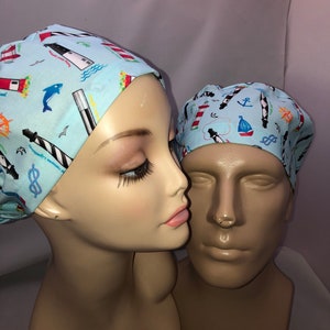 May include: Two surgical caps with a nautical theme. The caps are light blue with a white background and feature lighthouses, boats, anchors, and other nautical symbols.