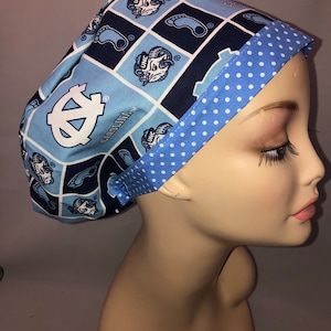 May include: A blue and white patterned surgical scrub hat with a white polka dot trim. The hat features a repeated pattern of the UNC Tar Heels logo and a footprint.
